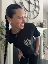 a woman wearing a black t - shirt smiling in front of a clock